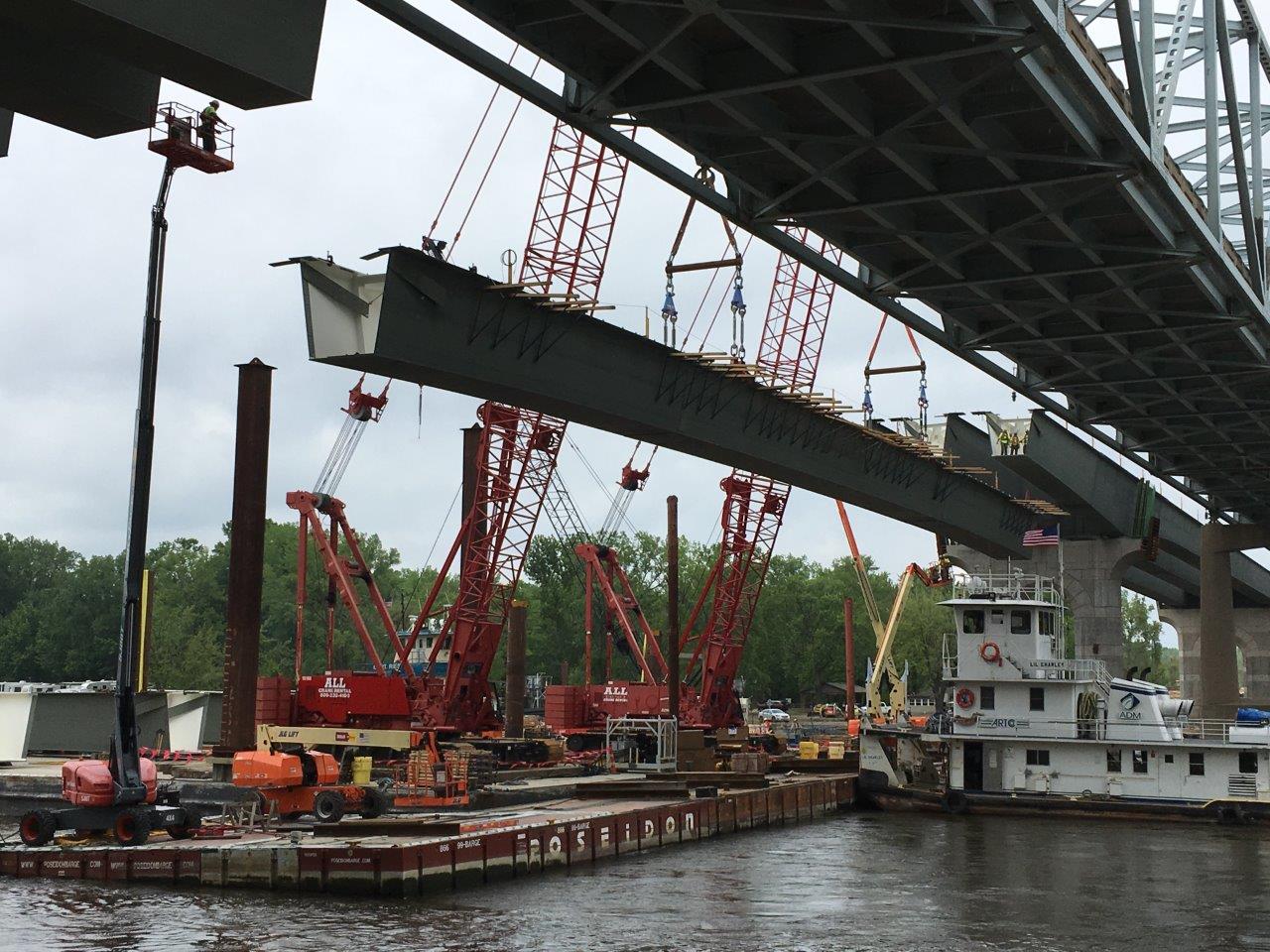 A river barge with cranes on it, lifting the bottom piece of a bridge into place.
